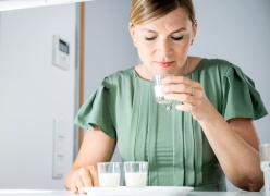 Eine Frau in einem grünen Kleid riecht an einer Aromenprobe, eine milchige Flüssigkeit in einem kleinen Shotglas. Vor ihr stehen 2 weitere Proben zum nächsten Vergleich.