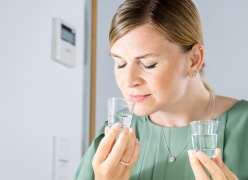 A woman is test tasting flavour samples in a clear liquid in shot glasses. She has her eyes closed and is fullly engaged in the flavour.