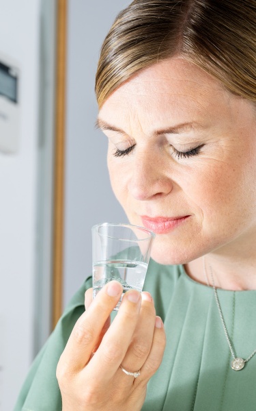 A woman is test tasting flavour samples in a clear liquid in shot glasses. She has her eyes closed and is fullly engaged in the flavour.