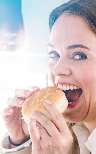 Woman biting into a burger bun at the taste-excellence centre.