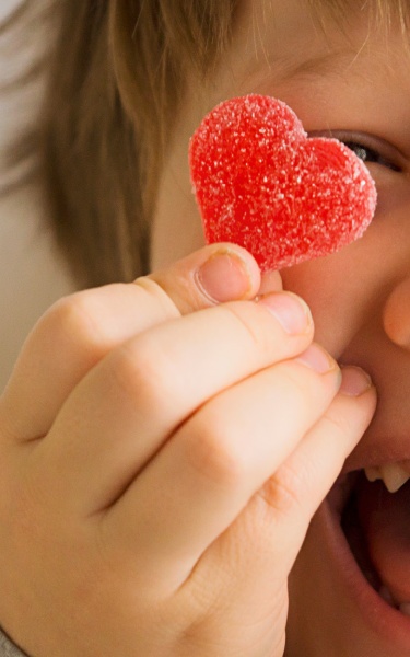 Young child holding up two red candy hearts in front of their eyes with a cheeky smile.