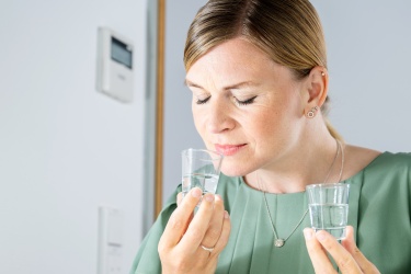 A woman is test tasting flavour samples in a clear liquid in shot glasses. She has her eyes closed and is fullly engaged in the flavour.