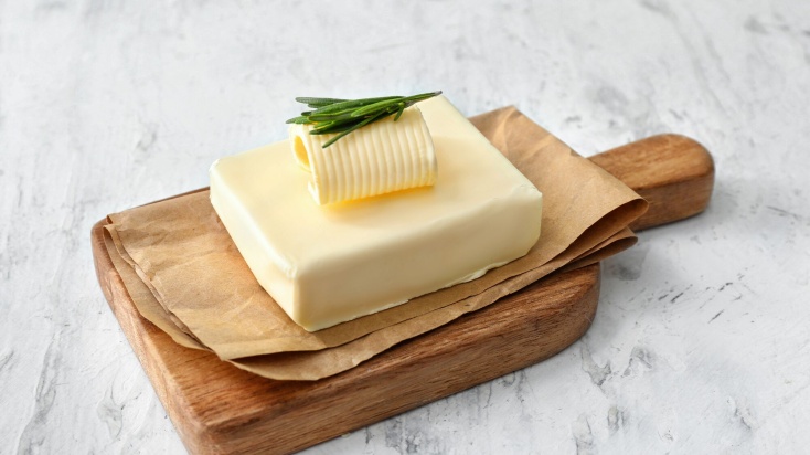 A pice of butter on a wooden cutting board topped with hint of parsley