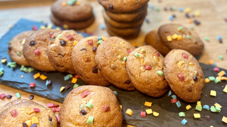 A pile of chocolate chips cookies with colourful sprinkles around them.