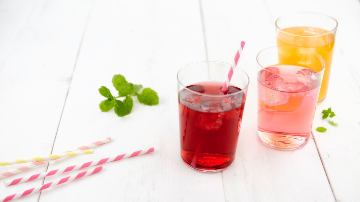 Three glasses of sparkling juices in dark red, ligh red and yellow with straws.