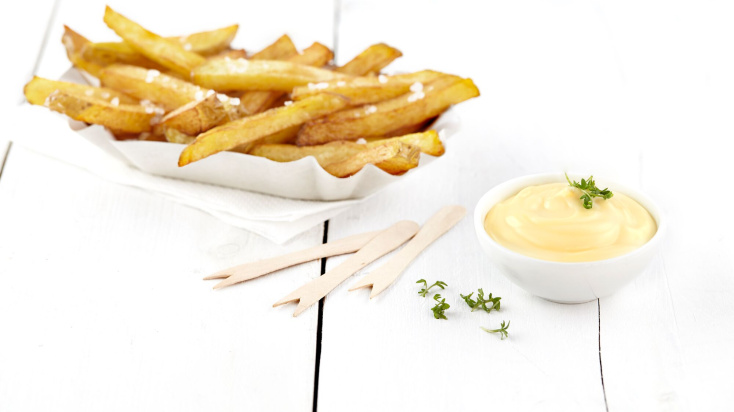 A bowl of creamy mayonnaise next to tray of crispy french fries.