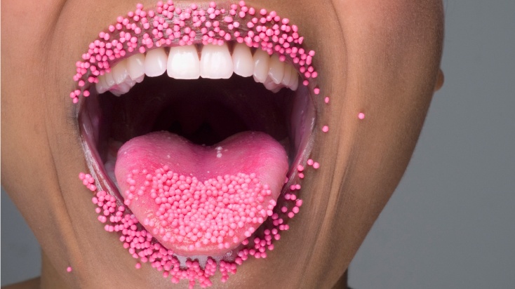 a woman sticking out her tongue with pink sugar pearls on it