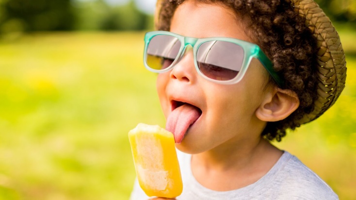 Child licking orange water ice popsicle