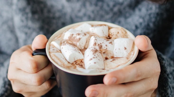 Two hands cupped around a cup of hot chocolate with marshmellows