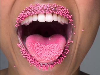 Woman sticking out her pink tongue with pink sugar pearls on her lips