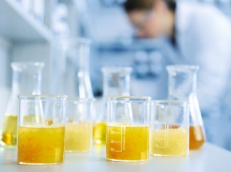 Flavourist working in a flavouring lab. In front of her there are glasses with liquid in different orange shadings. 