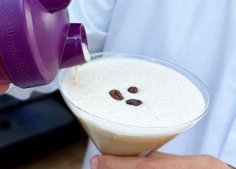 A cream coffee drink is poured into a martini glas from a purple OlrbichtArom shaker.